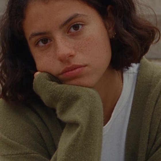 A girl with her hand up, sitting on steps